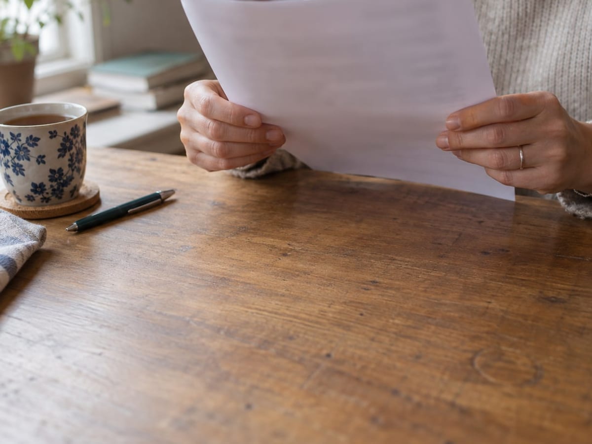 Une femme relit un courrier à sa table, une tasse de thé posée à côté